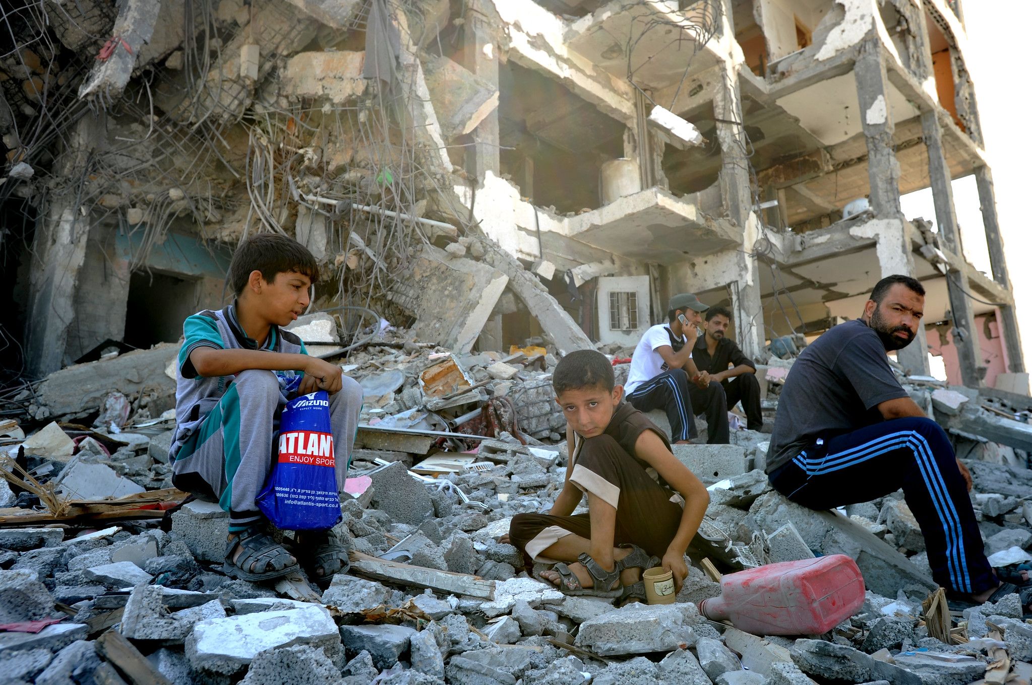 children and man sitting on rubble of bombed building in Gaza