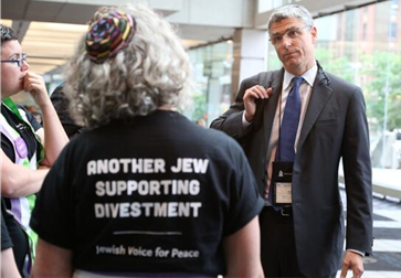 Photo of two people talking - one person with t-shirt stating "another Jew supporting divestment"