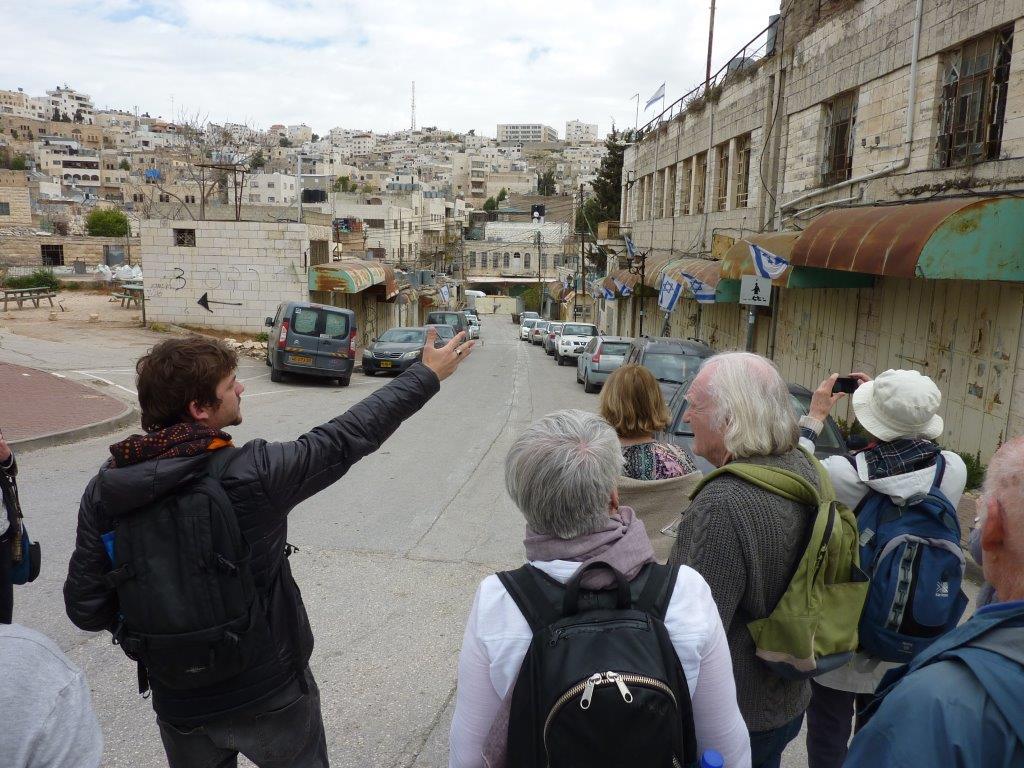 Tour guide showing people an abandoned Palestinian street with Israeli flags hanging along it.