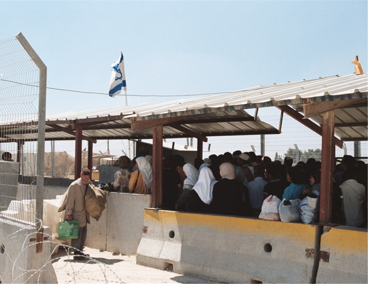 Palestinian people stnading under corragated iron as a checkpoint