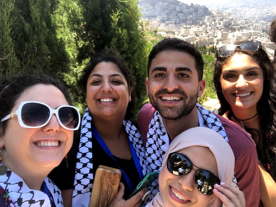 Five young Palestinians smiling with a Palestinian city in the background