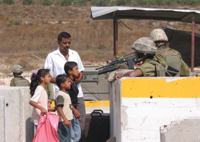 Photo of Palestinian children at a checkpoint with a solider with a gun pointed at them