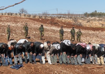 Photo of men praying in dry field with Israeli soldiers